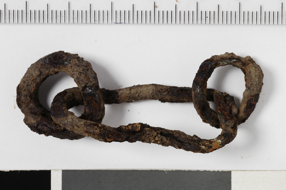MÅL: L. 6, 2 CM, EN STOR FLATTRYKT RING OG ENN MINDRE RING I HVER ENDE AV DENNE. FRAMSTILT AV JERNTRÅD LAGT OM HVERANDRE I SKJØTENE.