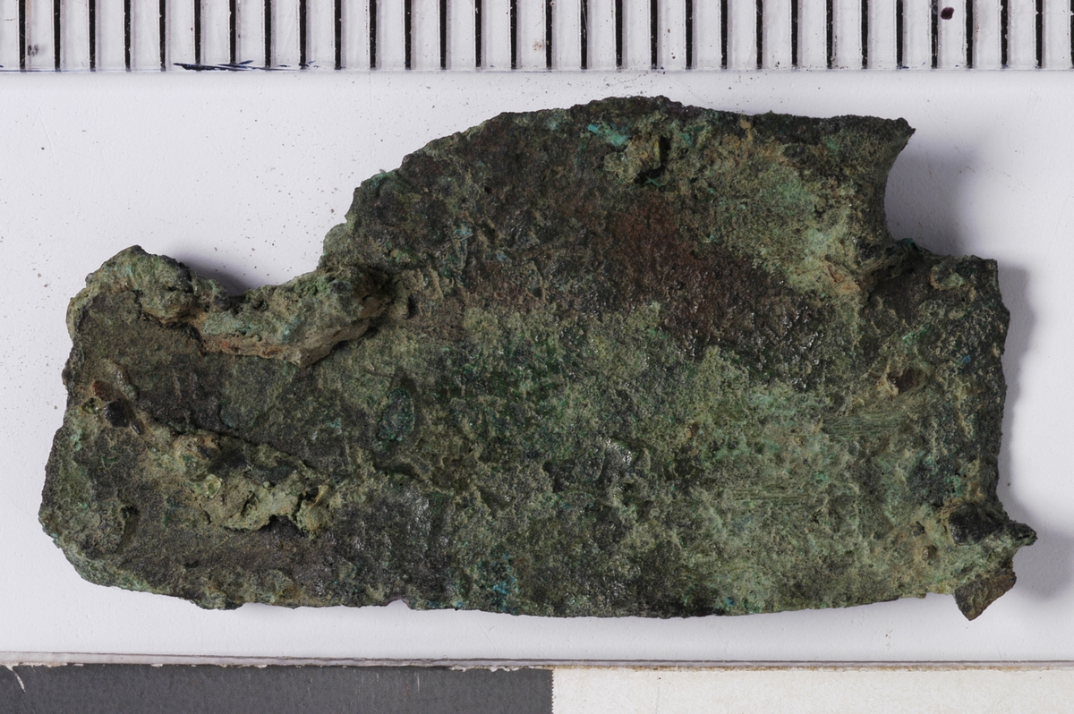 MÅL: L. 2, 8 CM H. 1, 5 CM, UREGELMESSIG, BULKET STYKKE AV TYNN BRONSEPLATE. MULIG SPOR ETTER NAGLEHULL.
