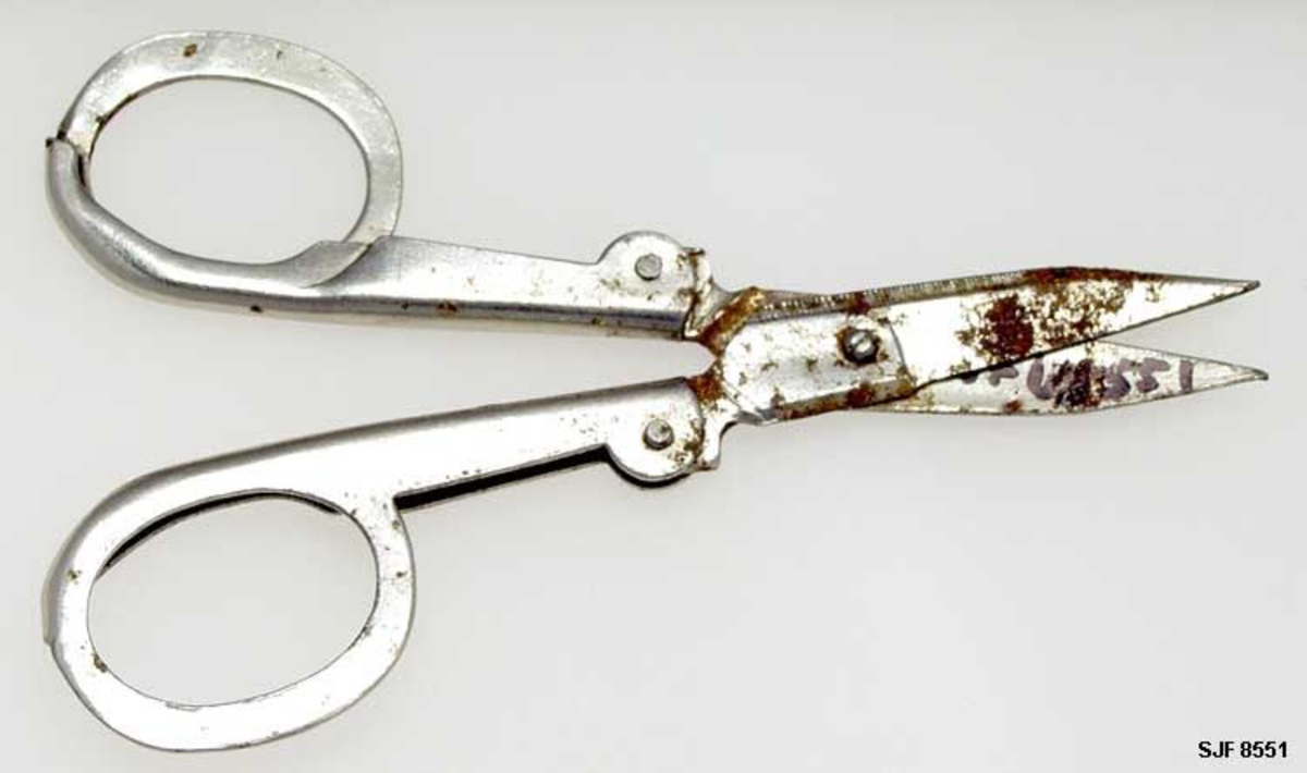 Lita, sammenleggbar saks, muligens fra stoppesett for reisebruk, kanskje også anvendelig til klipping av negler. I utfoldet stand er saksa cirka 10,5 centimeter lang. Bladene er 3,4 centimeter lange, målt fra sentrum av skruen som hengsler dem sammen, cirka 5,5 centimeter lange målt mellom bladspissene og endene der hendlene er pånaglet. Bladene har svakt konvekst buete, men nesten rette egglinjer. Nakkepartiene er konvekse, med riflete skråfaser. Hendlene er stanset ut av ei 1 millimeter tjukk stålplate og delvis falset slik at de fremre enden omslutter de bakre endene av bladstålene. Her er komponentene sammenføyet ved hjelp av nagler i overgangsonene mellom blader og armer. Dette gjør at bladet kan bøyes inn i øverste del av armen (lommekniv-prinsippet). Hendlene har ovale fingerhull. Den ellers blanke metalloverflata har noen små rustflekker.