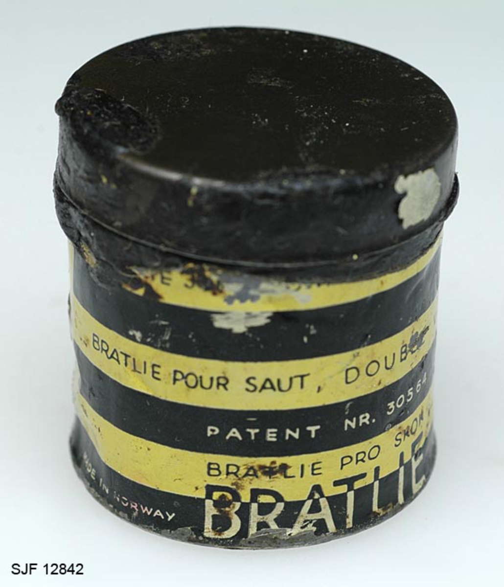 Boksen med skismurning har sylindrisk form. Den består av en metallsylinder og et lokk. Utenpå metallsylinderen er det påklistret en etikett hvor det bl. a er bilde av en skihopper som utfører et svev (øvrig informasjon fra etiketten er ført inn i feltet for påført tekst). 
Teksten som er påskrevet øverset på boksen er nesten helt borte, slik at det er umulig å tyde hva som har stått der. Etter hvert som man har brukt smurning, har det vært nødverndig å rive av deler av boksen, og dermed har deler av den påførte teksten på boksen fulgt med. 