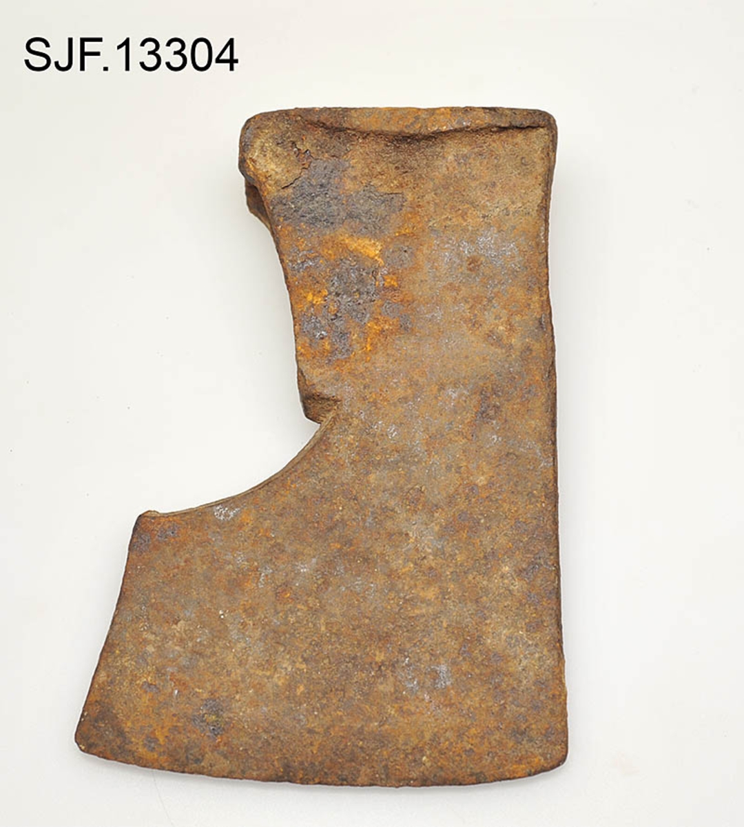 Økseblad uten skaft.  Redskapet er overført fra Borgarsyssel museum i Sarpsborg, dessverre uten proveniensinformasjon ut over at den skal være brukt i Østfold. 

Øksa er smidd, antakelig med innlagt stål i eggpartiet, men ettersom overflata er dekt av rust er det vanskelig å verifisere dette uten å foreta oppsliping.  Dette framstår som et forholdsvis tungt og bredt økseblad.  Med denne bladbredden har det neppe har vært beregnet på hogst, men det kan naturligvis ha vært brukt til barking, men også til ymse håndverksaktiviteter.  Den øvre delen (omkring øyet og nakken) er preget av slitasje.  Det nedenforliggende bladet er noe bredere.  Nakkedelen har opprinnelig vært flat og rektangulær, men den er brukt som hammer, noe som har ført til at godset er noe deformert og at det har dannet seg "skjegg" langs langsidene.  Øyet (skafthullet) har et dråpeformet tverrsnitt (cirka 5, 2 X 2, 6 centimeter). Godset mellom øyet og hammerflata på øksenakken er sprukket, noe som kan ha vært årsak til at redskapet ble kassert.  Eggdelen har betydelig større bredde enn nakkedelen. 