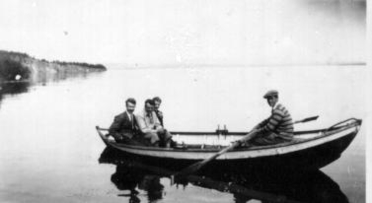 4 menn i robåt på Mjøsa utenfor Kleven. Storbergsodden i bakgrunn.