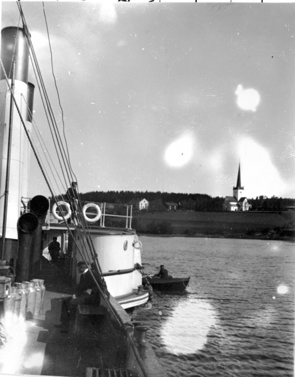 Mjøsbåten D.S. Kong Oscar på vei ut fra Ringstrand brygge ved Ringsaker kirke. Mjølkekjeler ombord. Robåt ved siden.