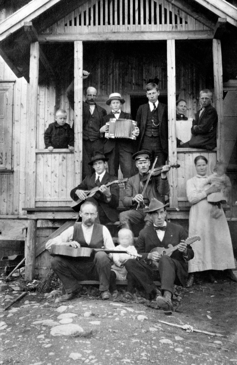 12 voksne og barn i trapp på ukjent sted. med musikkinstrumenter, trekkspill, fele, gitar og mandolin.