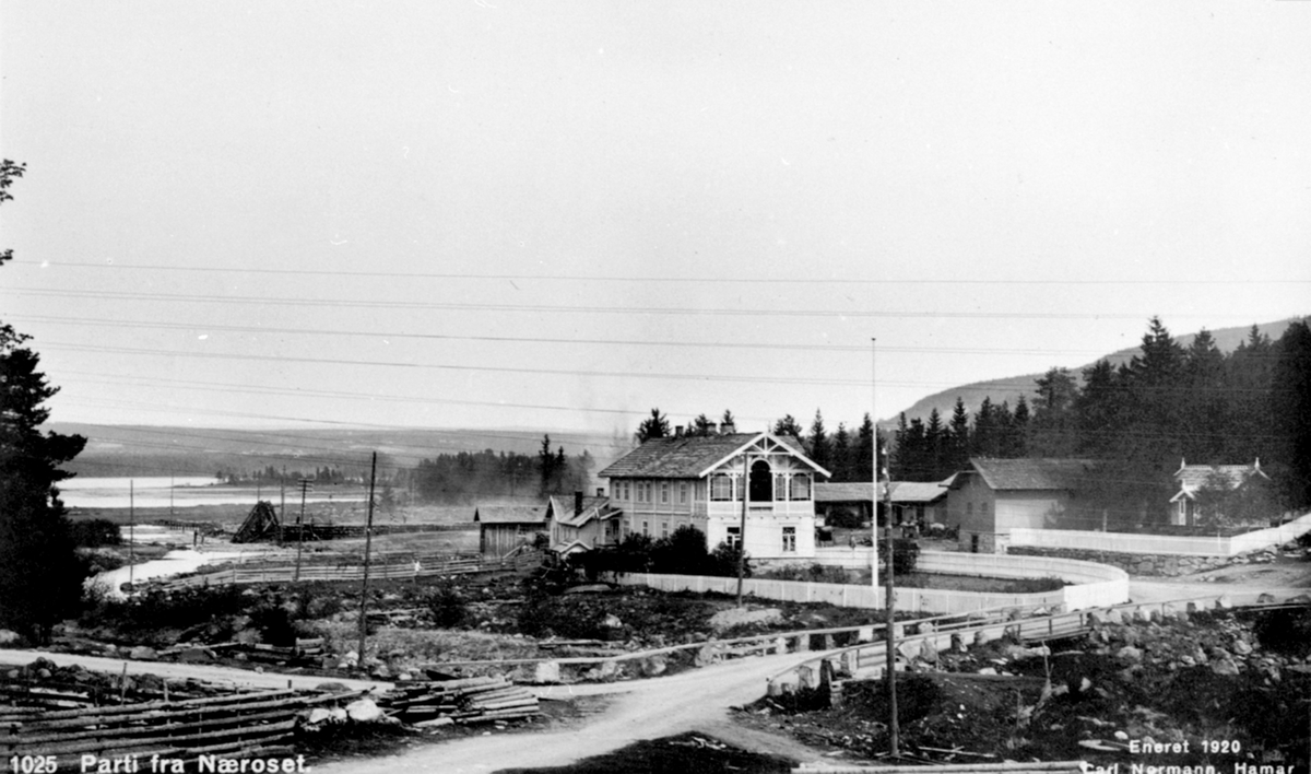 Postkort, Parti fra Næroset, Ringsaker. Harby's landhandler, Fagernes. Fra venstre er skåle, bakeri, hovedbygning med butikk, fjøs-stall, lagerbygning, lekestue med to rom, lof og veranda, gåsehus foran bakeri. En bru over utgravd kanal og bru over elva mot butikken. I bakgrunnen ser en tømmerkjerraten til Moelven Cellulosefabrikk.