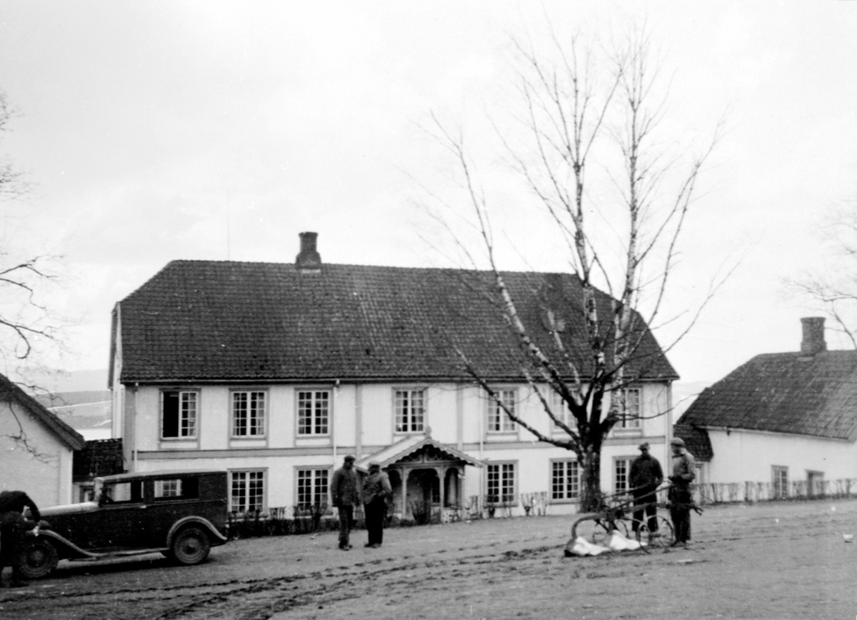 Hovedbygningen på Hovelsrud, Helgøya sett fra vegen. Bil og 5 karer i forgrunnen. Plog.
