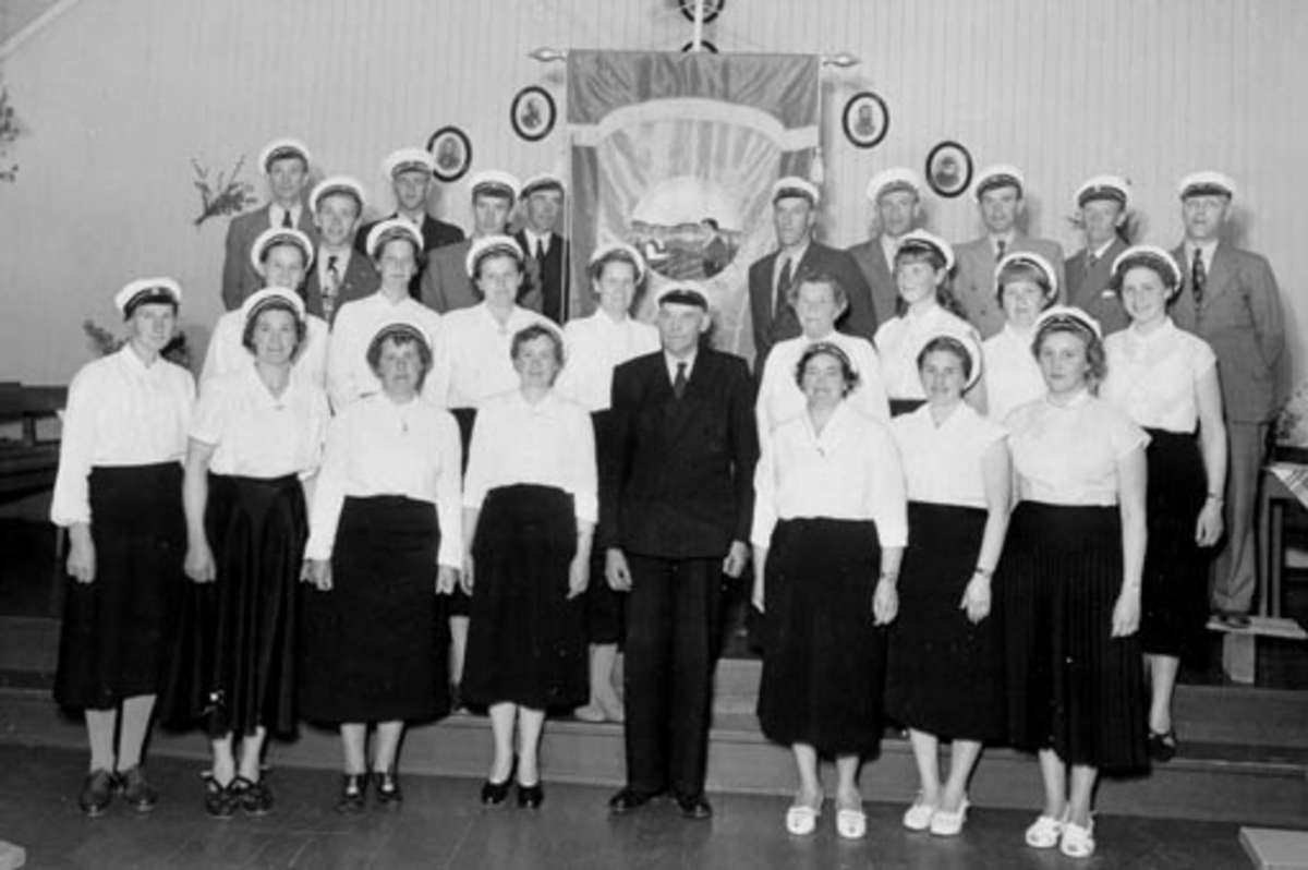Blandet sangkor. Furnes sangforening med fane, Ringsaker. Se HHB-00165 for original. 
Furnes sangforening 1956
Bildet er tatt i forbindelse med innvielse av ny fane i 1956. Det skjedde på Betania bedehus hvor koret holdt øvelser den gangen. Første rekke f.v. Lovise Røsbak, Marthe Marken, Sigrid Buenget,  Solveig Backe, dirigent Gunnar Fredhjem, Lisbeth Haugen, Janne Enger, Ingrid Heggelund. Midtre rekke, Astrid Hangenholen, Berthe Arneberg, Marthe Hegsvold, Marthe Mikkelsen, Nora Fredhjem, Arnhild Arneberg, Gerd Hansen, Karin Turi Brun. Bakre rekke, Torbjørn Skogli, Oskar Engebakken, Arve Andersen, Nils Høisveen, Ivar Hegsvold, Reidar Arneberg, Henry kirkeby, Arne Kirkeby, Alf Sandli, Sverre Opsal.