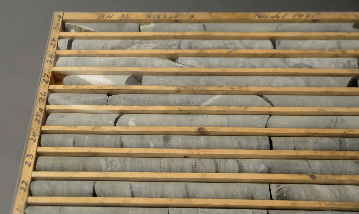 Rektangulær, nummerert, ganske flat kasse med systematisk organiserte nummererte rom for bergprøver. Kassen inneholder ti avlange rom, og i hvert ligger bergprøver.