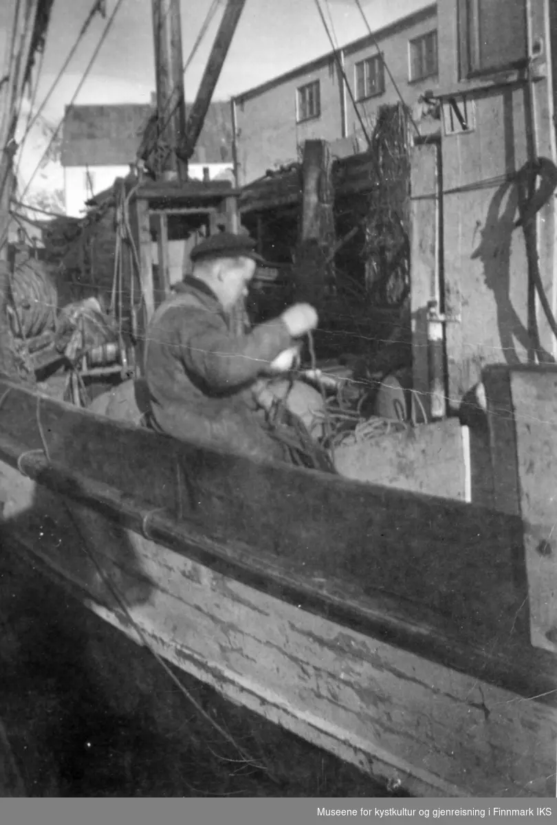 Olav Jensen etterser snurrevadbruket ombord i  Mk "Skarholmen" av Kongsfjord. Riksheimkaia i Svolvær. Værmerket N på styrehuset, ca 1952