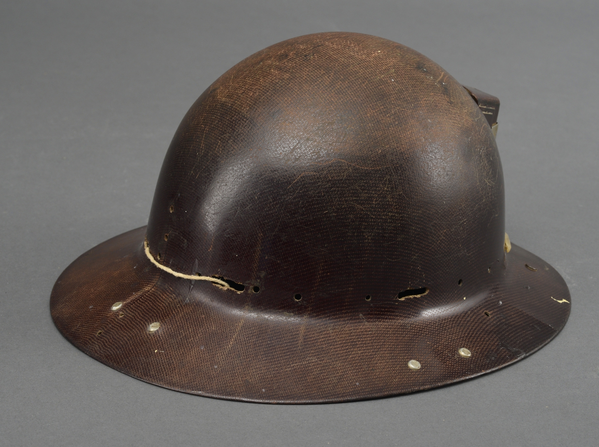 Gruvehjelm med påsatt del avplast og jern for feste av skjerm på undersiden av bremmen. Lampefeste på front- og ledningsfeste bak på hjelmen.