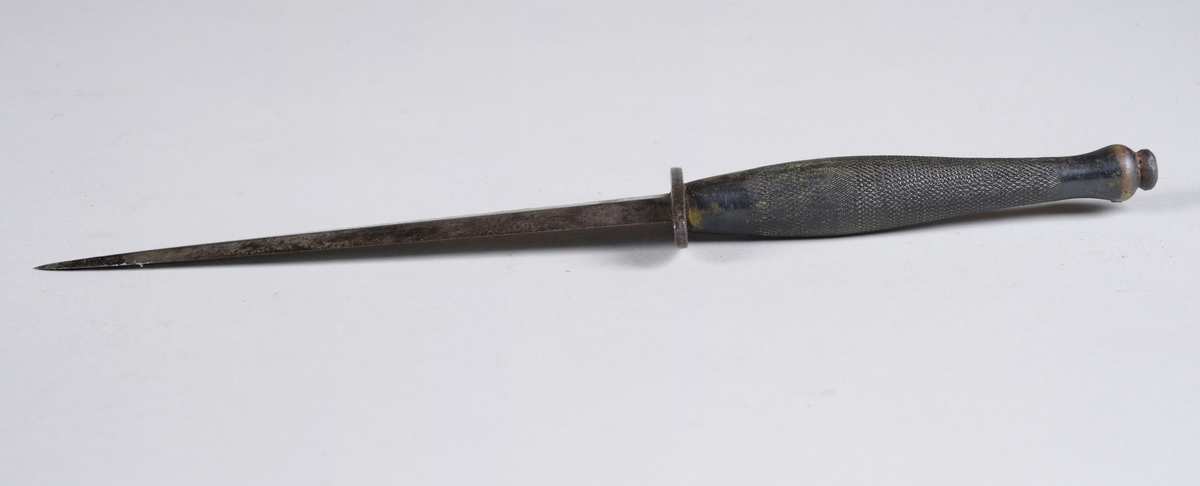 Dolk av jern i lærhylster. 
Hylsteret er forsterket i spissen og kan festes i belte. Dolken har et ruglete håndtak og et toegget blad med midtribbe.