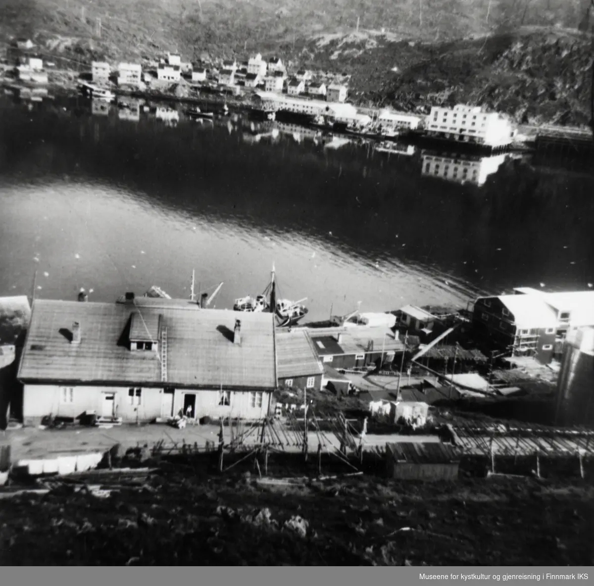 Honningsvåg. Richard Floers fiskebruk A/S i Storbukt. I bakgrunnen Finotro og deler av bebyggelsen. 1950-tallet.