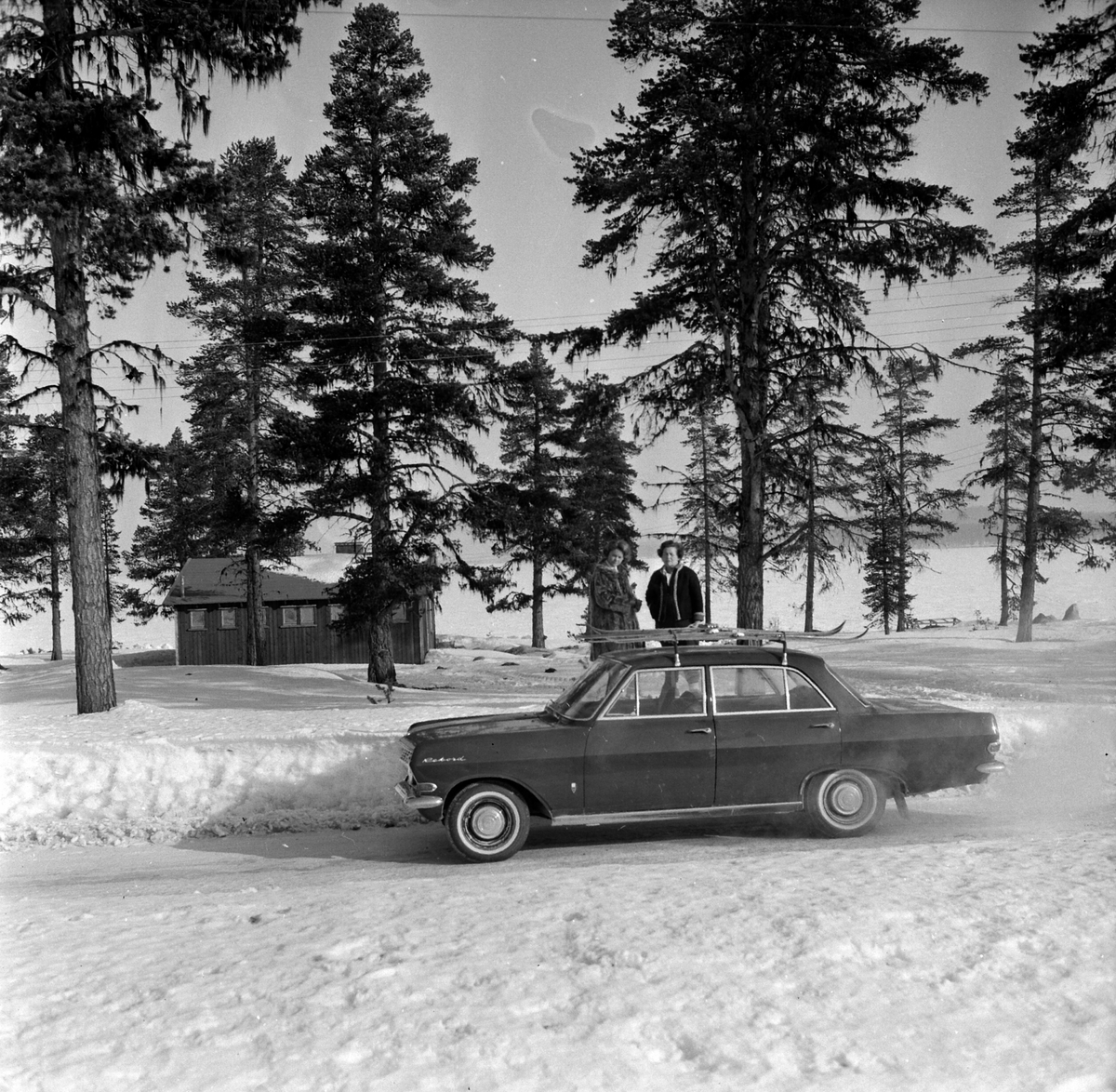 Opel Rekord modell A 1963-65. (Rekord B 1966 var identisk men hadde runde baklykter). Skistativ, to ukjente kvinner. med ski på taket.