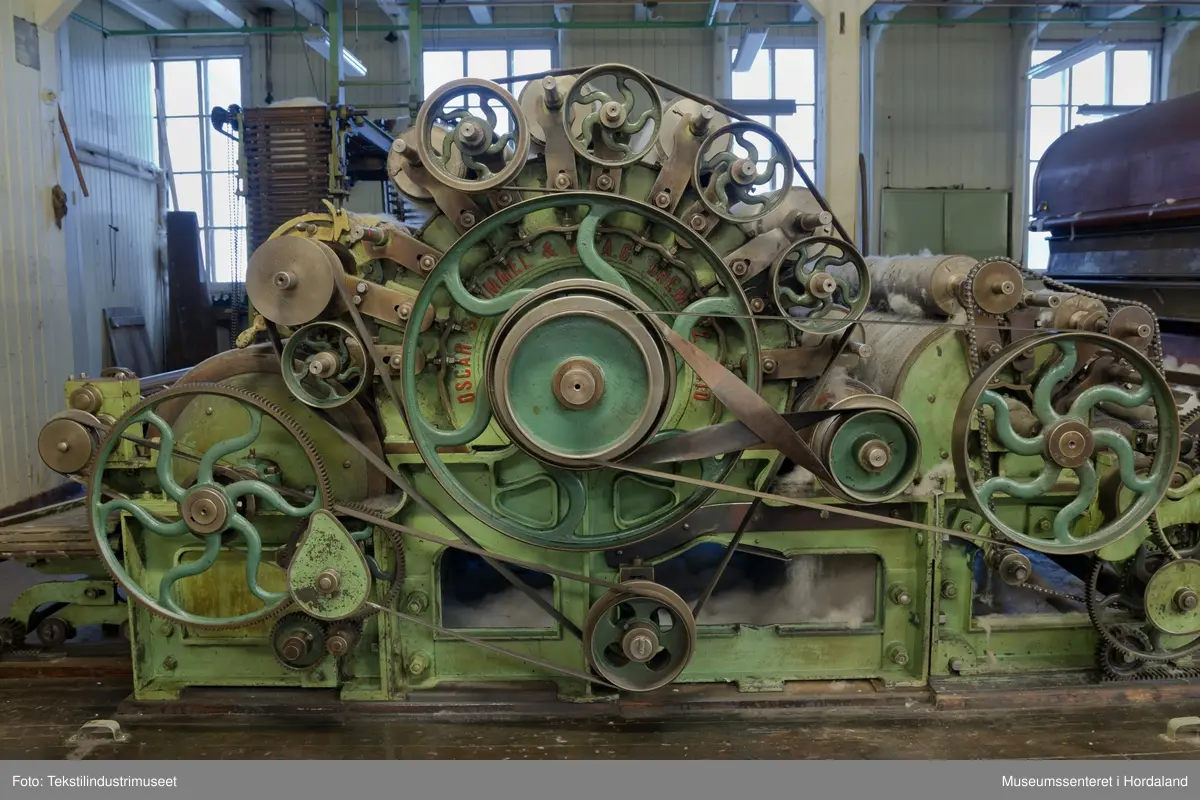 Kardeverk med tre kardemaskiner som er kopla saman og arbeider i serie, frå Oscar Schimmel & Co i Chemnitz, Tyskland. Frå ullinntaket i eine enden av maskina, blir ulla ført over valsar med metallkardar på, som fjernar ureinheiter og løyser opp floker i ullfibra. Ulla blir karda ein gong før den går over eit transportband i tre, blir snudd og karda to gonger til før det karda ullfloret går gjennom ein flordelar som deler det opp i remser. Remsene blir rulla opp på store metallspolar, og blir då kalla forgarn. I forgarnet ligg alle ullfibra etter kvarandre, men garnet er utan styrke og må spinnast for å bli til brukbart garn. 

Maskina var i bruk på Salhus Tricotagefabrik (1859-1989), og hadde her internt maskinnummer 5. Kardeverket står i hesteskoform med ullinntaket og ei kardemaskin på ei sida, to kardemaskiner og flordelaren på andre sida, og eit transportband i tre som bindeledd mellom dei to. Kardeverket blir drive av tre elektriske motorar som er festa til golvet på innsida av 'hesteskoen'. Maskina er grønmåla, med mange dekorative tannhjul med bua eiker, typisk for maskiner frå rundt 1900.

Det har seinare blitt montert ein støvsugar på kardeverket, som syg opp støv ved flordelaren, og transporterer det tilbake til ullinntaket. Røyra til støvsugaren ser 'heimelaga' ut, og er sett saman med bl.a. teip og ulike typar røyr.