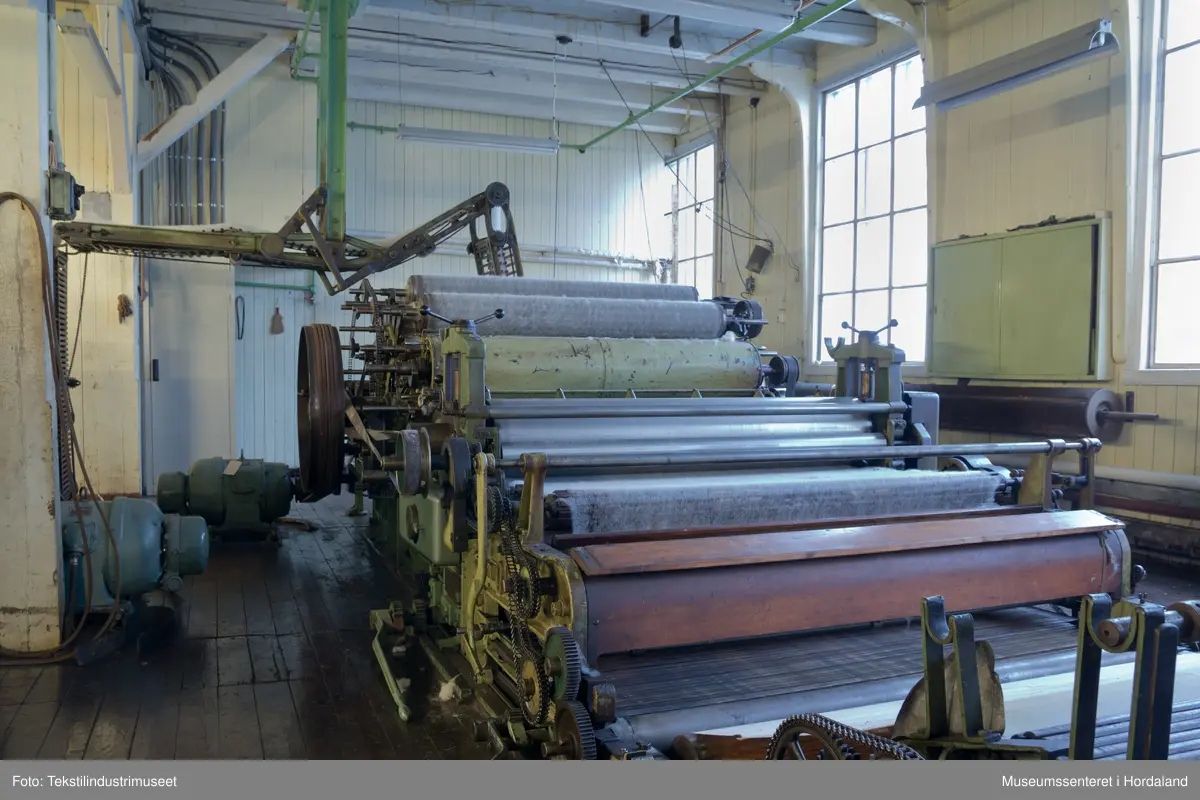 Kardeverk med tre kardemaskiner som er kopla saman og arbeider i serie, frå Oscar Schimmel & Co i Chemnitz, Tyskland. Frå ullinntaket i eine enden av maskina, blir ulla ført over valsar med metallkardar på, som fjernar ureinheiter og løyser opp floker i ullfibra. Ulla blir karda ein gong før den går over eit transportband i tre, blir snudd og karda to gonger til før det karda ullfloret går gjennom ein flordelar som deler det opp i remser. Remsene blir rulla opp på store metallspolar, og blir då kalla forgarn. I forgarnet ligg alle ullfibra etter kvarandre, men garnet er utan styrke og må spinnast for å bli til brukbart garn. 

Maskina var i bruk på Salhus Tricotagefabrik (1859-1989), og hadde her internt maskinnummer 5. Kardeverket står i hesteskoform med ullinntaket og ei kardemaskin på ei sida, to kardemaskiner og flordelaren på andre sida, og eit transportband i tre som bindeledd mellom dei to. Kardeverket blir drive av tre elektriske motorar som er festa til golvet på innsida av 'hesteskoen'. Maskina er grønmåla, med mange dekorative tannhjul med bua eiker, typisk for maskiner frå rundt 1900.

Det har seinare blitt montert ein støvsugar på kardeverket, som syg opp støv ved flordelaren, og transporterer det tilbake til ullinntaket. Røyra til støvsugaren ser 'heimelaga' ut, og er sett saman med bl.a. teip og ulike typar røyr.