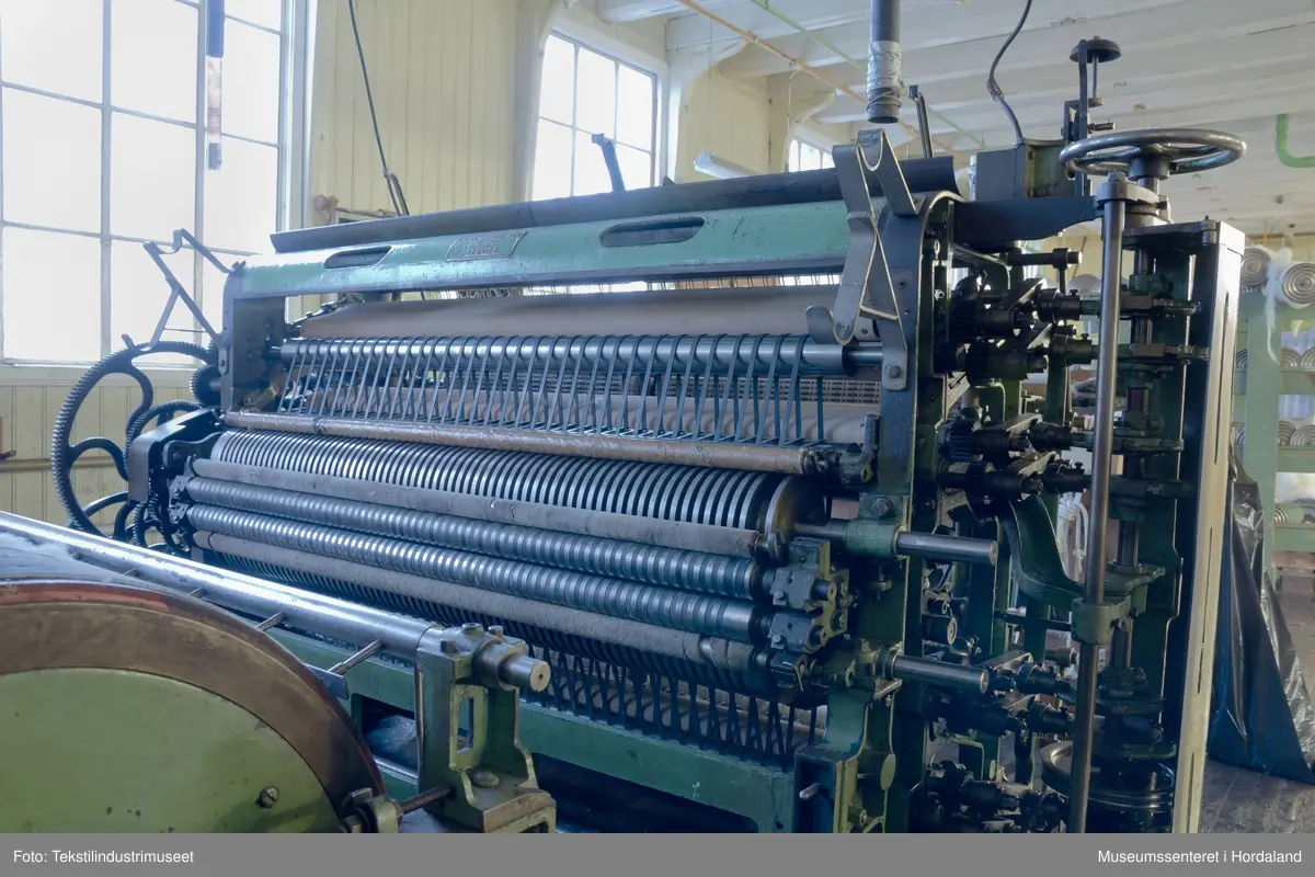 Kardeverk med tre kardemaskiner som er kopla saman og arbeider i serie, frå Oscar Schimmel & Co i Chemnitz, Tyskland. Frå ullinntaket i eine enden av maskina, blir ulla ført over valsar med metallkardar på, som fjernar ureinheiter og løyser opp floker i ullfibra. Ulla blir karda ein gong før den går over eit transportband i tre, blir snudd og karda to gonger til før det karda ullfloret går gjennom ein flordelar som deler det opp i remser. Remsene blir rulla opp på store metallspolar, og blir då kalla forgarn. I forgarnet ligg alle ullfibra etter kvarandre, men garnet er utan styrke og må spinnast for å bli til brukbart garn. 

Maskina var i bruk på Salhus Tricotagefabrik (1859-1989), og hadde her internt maskinnummer 5. Kardeverket står i hesteskoform med ullinntaket og ei kardemaskin på ei sida, to kardemaskiner og flordelaren på andre sida, og eit transportband i tre som bindeledd mellom dei to. Kardeverket blir drive av tre elektriske motorar som er festa til golvet på innsida av 'hesteskoen'. Maskina er grønmåla, med mange dekorative tannhjul med bua eiker, typisk for maskiner frå rundt 1900.

Det har seinare blitt montert ein støvsugar på kardeverket, som syg opp støv ved flordelaren, og transporterer det tilbake til ullinntaket. Røyra til støvsugaren ser 'heimelaga' ut, og er sett saman med bl.a. teip og ulike typar røyr.