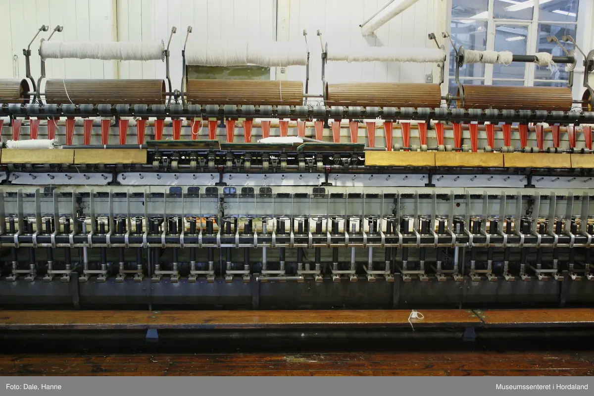 Elektrisk ringspinnemaskin (1958) frå det sveitsiske selskapet Rieter. Øvst på maskina plasserer ein spolane med forgarn frå kardemaskina. Reint teknisk er det tre hovudelement i spinninga:  forgarnet blir strukke, tvista (snodd) for å få meir styrke, før det ferdige garnet blir oppvikla på ein spole eller 'spinnepipe'. Tråden går under eit transporthjul i tre, gjennom støypte løpegangar og vidare nedover: Garnet blir snodd ved at garnet passerer ein løpar som beveger seg på ein ring, før det blir samla på ein sylindrisk metallspole. Det er ei rekkje små støvsugarar langs heile maskina, små røyr som stikk ut over spolane. Desse syg til seg støv og/eller tråden viss den ryk, for å unngå at den kjem inn i maskina. Trådrestar og støv blir samla opp i eit oppsamlingskammer på venstre sida av maskina. Der er det òg ein målar som måler kor mykje maskina spinner.

Drivverket og ein stjernemotor sit på høgre sida av maskina. På sida står det "Rieter" i raudt, og det er to målarar som måler omdreiingar/hastigheit på maskina. Det er ei rekkje med 136 koner på kvar side. Maskina kan byggjast på i seksjonar, og slik utvidast etter behov, noko som er vanleg for spinne- og spolemaskiner.