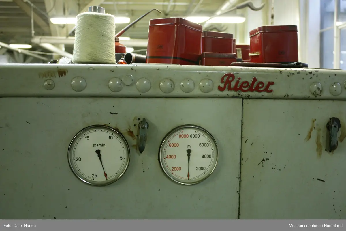 Elektrisk ringspinnemaskin (1958) frå det sveitsiske selskapet Rieter. Øvst på maskina plasserer ein spolane med forgarn frå kardemaskina. Reint teknisk er det tre hovudelement i spinninga:  forgarnet blir strukke, tvista (snodd) for å få meir styrke, før det ferdige garnet blir oppvikla på ein spole eller 'spinnepipe'. Tråden går under eit transporthjul i tre, gjennom støypte løpegangar og vidare nedover: Garnet blir snodd ved at garnet passerer ein løpar som beveger seg på ein ring, før det blir samla på ein sylindrisk metallspole. Det er ei rekkje små støvsugarar langs heile maskina, små røyr som stikk ut over spolane. Desse syg til seg støv og/eller tråden viss den ryk, for å unngå at den kjem inn i maskina. Trådrestar og støv blir samla opp i eit oppsamlingskammer på venstre sida av maskina. Der er det òg ein målar som måler kor mykje maskina spinner.

Drivverket og ein stjernemotor sit på høgre sida av maskina. På sida står det "Rieter" i raudt, og det er to målarar som måler omdreiingar/hastigheit på maskina. Det er ei rekkje med 136 koner på kvar side. Maskina kan byggjast på i seksjonar, og slik utvidast etter behov, noko som er vanleg for spinne- og spolemaskiner.