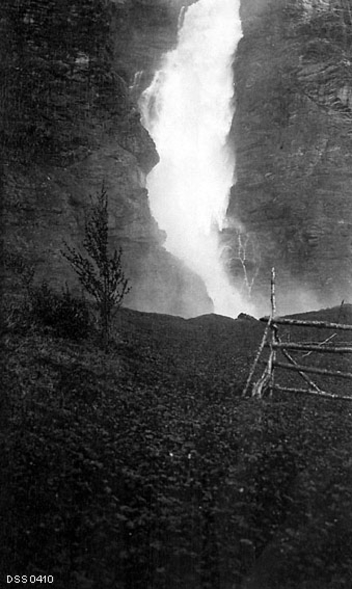 Mollisjokfossen i Nordreisa kommune i Troms, fotograftert fra en berghammer midt imot fossen.  På flata i forgrunnen sto det for øvrig ei rajehesje, som da fotografiet ble tatt ikke var belagt med noen form for stråfôr som skulle tørkes.  Fossen gikk kvitskummende nedover en forholdsvis bratt bergvegg.
