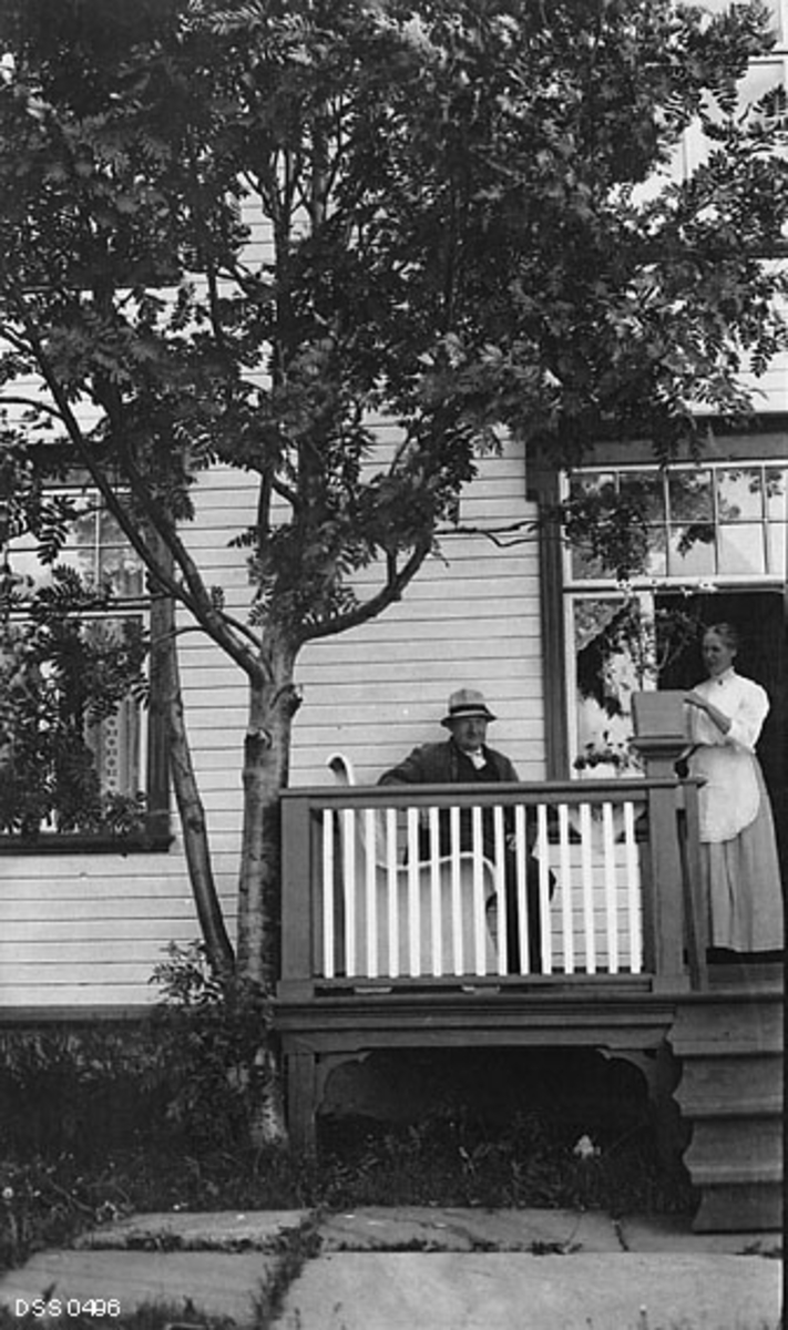 Emil og Agnes Kjeldsberg på verandaen utenfor villaen deres - Kjækan i Kvænangen i Troms.  Emil Kjeldsberg (1872-1956) er fotografert sittende på en kvitmalt benk, iført dress og lys sommerhatt med svart band rundt pullen.  Kona Agnes Kjeldsberg (1871-1933) sto og stelte med ei plante i ei firkantet potte da dette fotografiet ble tatt. Hun var kledd i kvit bluse og kvitt forkle over et noe mørkere skjørt.  Emil og Agnes hadde vært i California i perioden 1898-1909, der Emil var blant aktørene i det store gullrushet.  Han var antakelig blant dem som lyktes.  Fotografiet tyder i hvert fall på at Emil og Agnes må ha hatt råd til å bygge seg en bolig i amerikansk stil.  Huset var kvitmalt trevilla, kledd med horisontal skyggepanel.  Den hadde store jugendvinduer med omramminger som var malt i en mørk kontrastfarge til de kvite veggflatene. Den samme fargebruken finner vi igjen på verandaen, der rammeverket var mørkt, mens sprossene i rekkverket var kvite.  Marka framfor verandaen var hellelagt.  Etter hjemkomsten til Norge kalles Emil i noen kilder for "rentenist" - altså en person som levde på oppspart kapital.  I andre kilder, som på den statlige skogetatens kartotekkort til dette fotografiet, omtales han som "handelsmann".

Bygningen Emil og Agnes Kjeldsberg er fotografert foran på dette bildet var egentlig et eldre våningshus som var laftet av furutømmer. Tre-fire år før dette fotografiet ble tatt fikk de modernisert huset med ny ytterkledning, nye vinduer og dører, samt et tilbygg av granplanker i to etasjer.