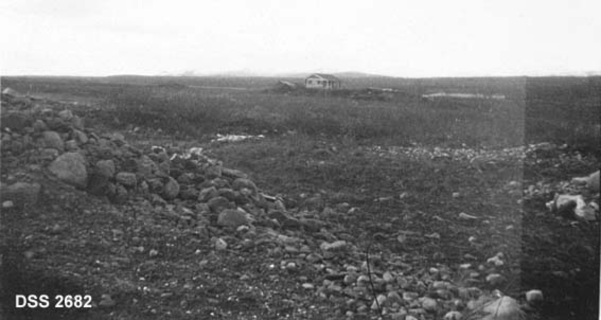 Hytte ved Lesjabekken.  Viddelandskap med mye stein i forgrunnen, hytta er såpass langt "inne i bildet" at det er vanskelig å danne seg noe inntrykk av eksteriøret. 