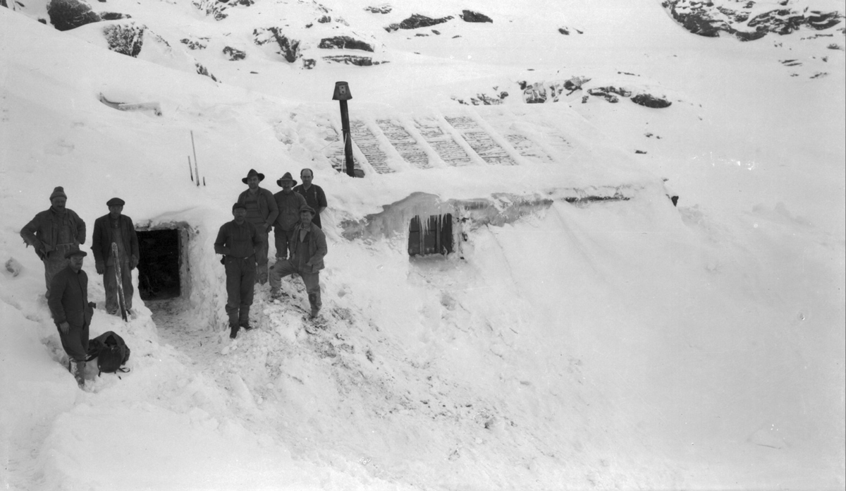 Anleggsarbeidarar framfor ei nedsnødd brakke ved Breiabu.