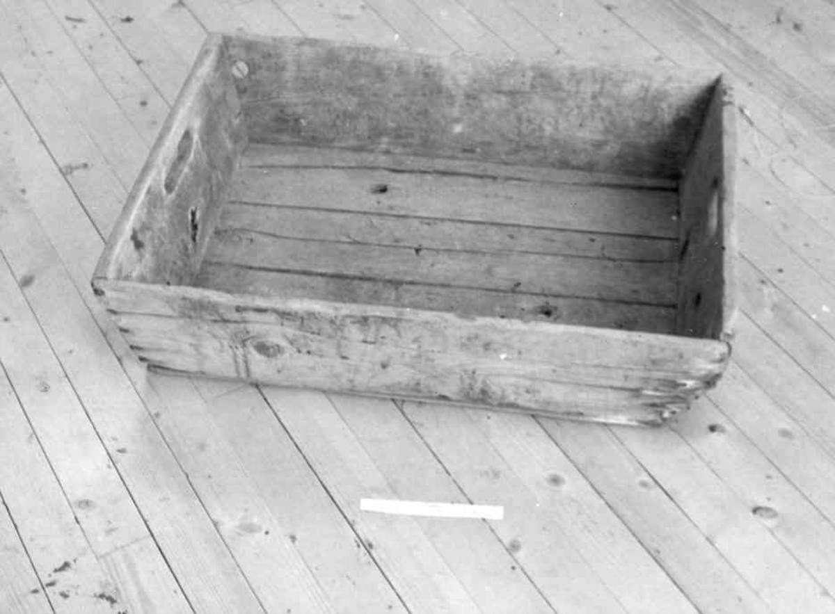 En firkantet kasse. Tappet sammen i hjørnene, har to hull for å bære kassen med.