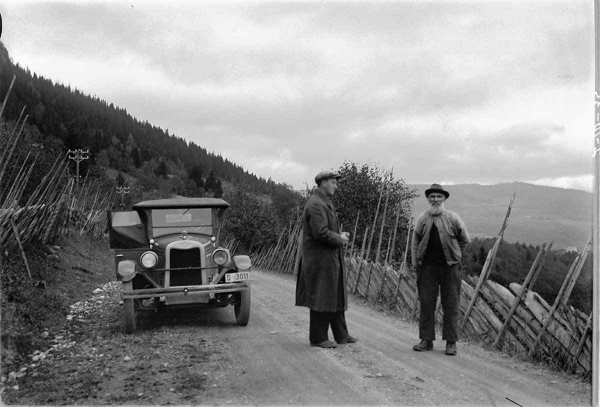 Gausdal, Lærer Karl Tallhaug t. v. den andre er ukjent, foran en bil med nummer D-3011, en Chevrolet 1925-26 modell. Grusveg, skigard, telefonstolper,
I Bilboken for Norge 1930 står registreringsnummeret på en Chevrolet personbil tilh. L. O. Lund, Vang. I Norges Bilbok 1935 på ditto 1926-modell, men eier var da Helmer Sørnes, Furnes.