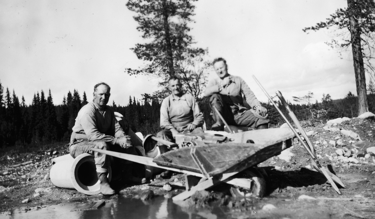 Vegbygging, vegarbeid, Trysil. Østby-Ljørdalen? Tre ukjente menn ved trillebår, redskaper, dreneringsrør. 
