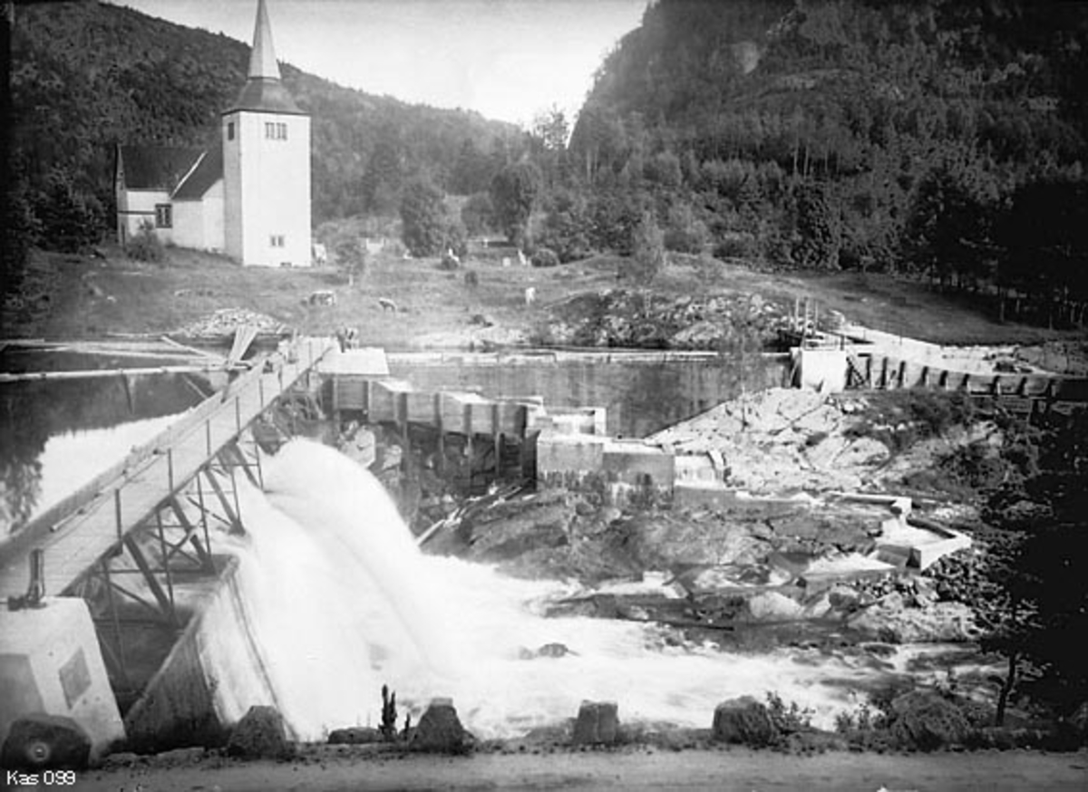 Foss med nåledam, laksetrapp og tømmerrenne i den delen av Gjerstadvassdraget i Aust-Agder som kalles Søndeledelva.  De nevnte kontruksjonene ble bygd i perioden 1905-1907, og de var følgelig ganske nye da dette fotografiet ble tatt i 1909.  Fotografen, ferskvannsbiologen Hartvig Huitfeldt-Kaas, var nok særlig opptatt av laksetrappa, som ble bygd i siksak oppover en bergrygg nedenfor fossen, med henblikk på å forlenge laksens vandringer oppover i vassdraget. Rester av denne laksetrappa skal ha stått inntil den ble revet vekk av en stor flom våren 2004.  Påfølgende sommer ble det bygd ny laksetrapp på samme sted.  Fløtingsløpet, med lense på oversida (til venstre) og tømmerrenne på nedsida (til høyre) var lagt i den østre delen av elveløpet.  Fotografiet er tatt fra det som i dag kalles Søndeledvegen (fylkesveg 418) på vestsida av vassdraget på tvers av elva mot (Indre) Søndeled kirke.  Dette er ei kvitkalket, murt korskirke med tårnoppbygg foran den fløyen som peker mot Søndeledelva.  Bygningen påståes å være bygd i perioden 1150-1200.