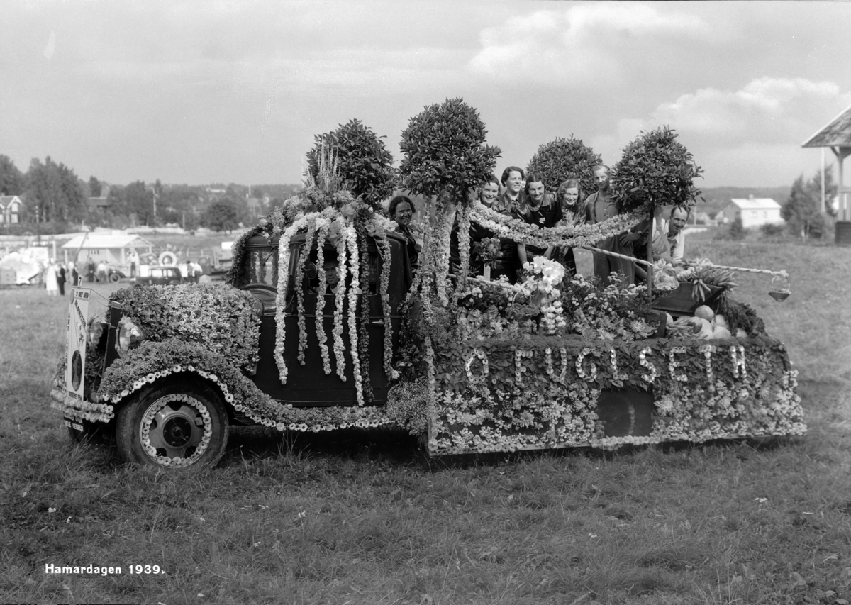 Hamar, Hamardagen 1939, lastebil med reklame for O. Fuglseth Handelsgartneri pyntet med blomster og grønnsaker, dagen var en todagers fest som samlet 50 000 mennesker, bilkortesje som representerte distriktets handel, håndverk og industri, på lasteplanet: Anna Blystad (f. Haugen), Martha Hansen, Aslaug Eggen (f. Arnkværn), Julie Eggen, Else Berg (f. Helmersen), garner Oddvar Eggen, gartner Nils A. Fuglseth,