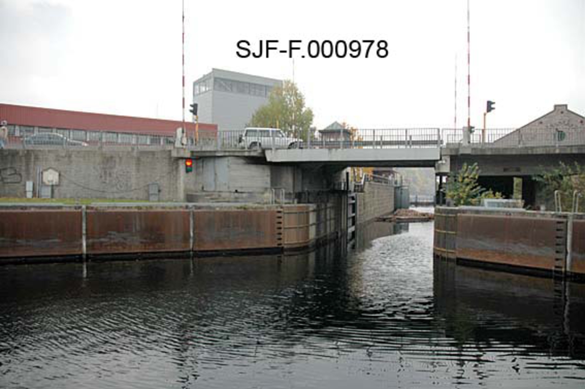 Skien sluse, sett ovenfra eller i strømretningen.  Fotografiet er tatt fra Hjellevannet, mot innløpet til slusene, gjennom øvre sluseport.  Murene mot vassdraget later til å være beslått med jernplater, som antakelig skulle bidra til at tømmerbuntene gled lett mot innløpet til slusene.  Over sluseinnløpet og øvre port er det ei heisbar vegbru med trafikklys og bommer på begge sider, slik at biltrafikken kan stanses når brua åpnes for å slippe gjennom store båter eller båter med høye master.  Tømmerbuntene kunne imidlertid gå gjennom slusa uten at dette skapte problemer for vegtrafikken. 