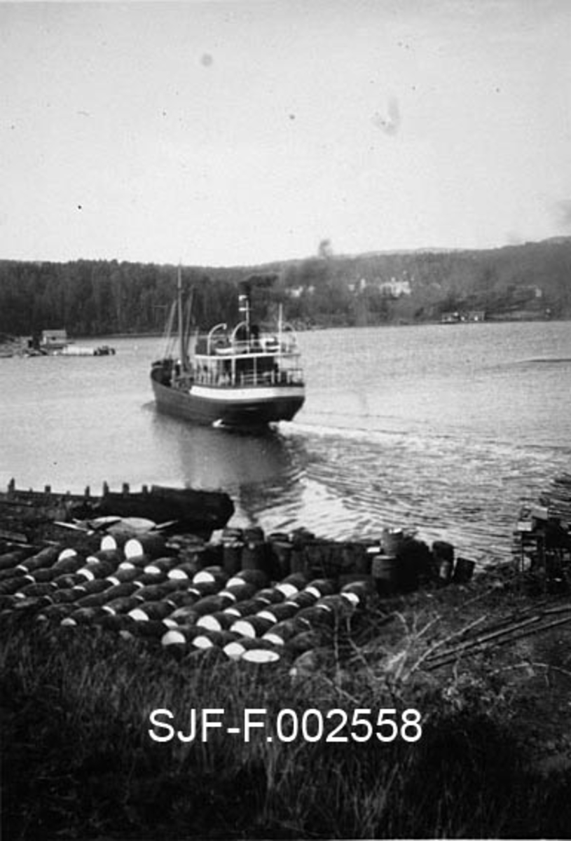 Dampbåten "Farmanden" fra Drammen, fotografert utenfor kaia til Schwencke & Co's Eftf. på Børholmen i Asker, like etter at den har lagt fra kai.  Båten har stålskrog som er malt i en mørk farge, riktignok med unntak av koøyefeltet på det overbygde akterdekket.  På dette bildet er det akterenden av båten som trer tydeligst fram.  På ei slette inne ved kaia ligger og står en mengde tønner.  Dette var emballasje til den produksjonsvirksomheten Schwencke & Co. drev på holmen. Bedriften produserte bek og andre tjæreprodukter. 