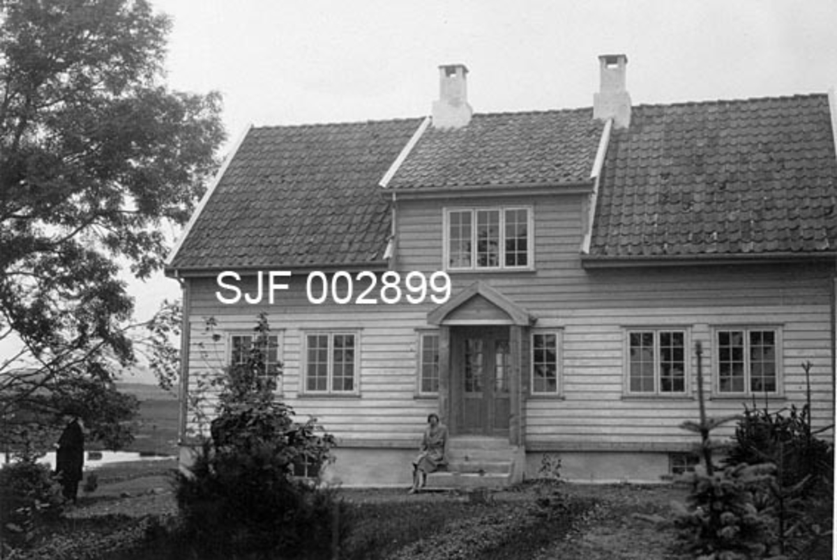 Våningshus på Rogaland Skogselskaps planteskole på Gruda i Klepp.  Fotografiet er tatt fra en slags hage mot det som antakelig var "fronten" på bygningen.  Eksteriøret var symmetrisk med inngang fra ei støpt trapp midt på fasaden.  Omkring den dobbelte inngangsdøra var det bygd et lite vindfang, og på taket over var det oppbygd en ark med pulttak.  Bygningen hadde klassiske smårutete vinduer, i hovedsak med to fag (grinder), men med tre fag i det vinduet som var montert på den nevnte arken.  Taket var tekket med krum teglstein og hadde to skorsteinspiper. Ei kvinne satt på trappa da fotografiet ble tatt.  En mann i mørk frakk og med hatt på hodet sto underet digert asketre til venstre for husets gavlvegg.  