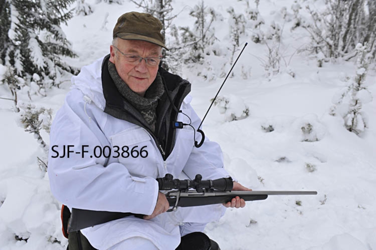 Fra opparbeidinga av tomteareal for Geithus Bruk på Modum i Buskerud. Dette bildet er sammensatt av to opptak, som begge er gjort i begynnelsen av april 1965. Da hadde man begynt å planere det arealet hvor industrihallen skulle reises. En del stein er samlet langs arealets ytterkant. Til venstre i bildet ligger et bolighus. Miljøet er ellers preget av skog.  Geithus Bruk var en virksomhet som kjøpte tømmer for barking og flishogging. Flisa ble levert til Skotselv Cellulosefabrikk i Øvre Eiker.