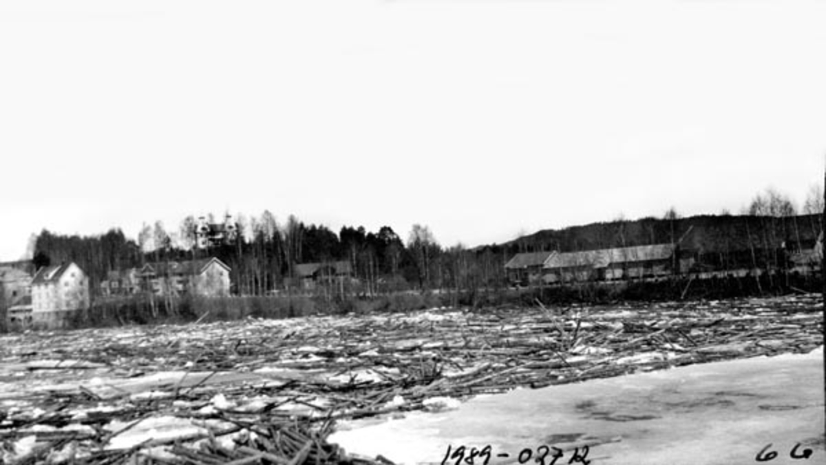 Isgang med mye fløtingstømmer ved Flisa bru i Åsnes i Hedmark våren 1928.  Fotografiet er tatt fra Glommas vestre bredd, over elveløpet mot et par gardstun på motsatt side.  I elva flyter isflak og tømmerstokker om hverandre. Våren 1928 gjorde isgangen store skader i Glommadalføret, særlig i Midt-Østerdalen. Men isen fulgte jo etter hvert med vannstrømmen sørover, og det tok tid før den smeltet. Derfor oppsto det problemer i Solør også, noe som framgår av dette utsnittet fra en reportasje i avisa Østlendingen samme dag som dette fotografiet skal være tatt:

«Den store tømmer- og ishaug som ligger fastskruet nedenfor Braskereidfoss vokser stadig, og det ligger nu lagret mangfoldige tusen tylfter lagret der. Isen ligger meget sterkt nedenfor, så haugen kommer sikkert ikke til å løsne så snart.
Den kritiske situasjonen ved Sanderbrua utløstes ved 10-tiden mandag kveld, da det lykkedes å bryte vei i isdammen. Men det var en voldsom påkjenning på brua da den løsnet.
Igår fortsattes sprengningen, og man fikk rent hovedløpet i Fulufjorden, så nu er det ingen overhengende fare. En stor tømmerhaug som gikk igår eftermiddag, tok med sig nedre lensefeste.
Forøvrig går Glåma full av is og tømmer, og den steg siste døgn atter en halv meter.»

På samme dato, 2. mai, 1928 vurderte Kongsvinger Arbeiderblad situasjonen ved Flisa slik: «Det er også isgang ved Flisa bru, men ingen fare hverken for flom eller annen skade ennå.»