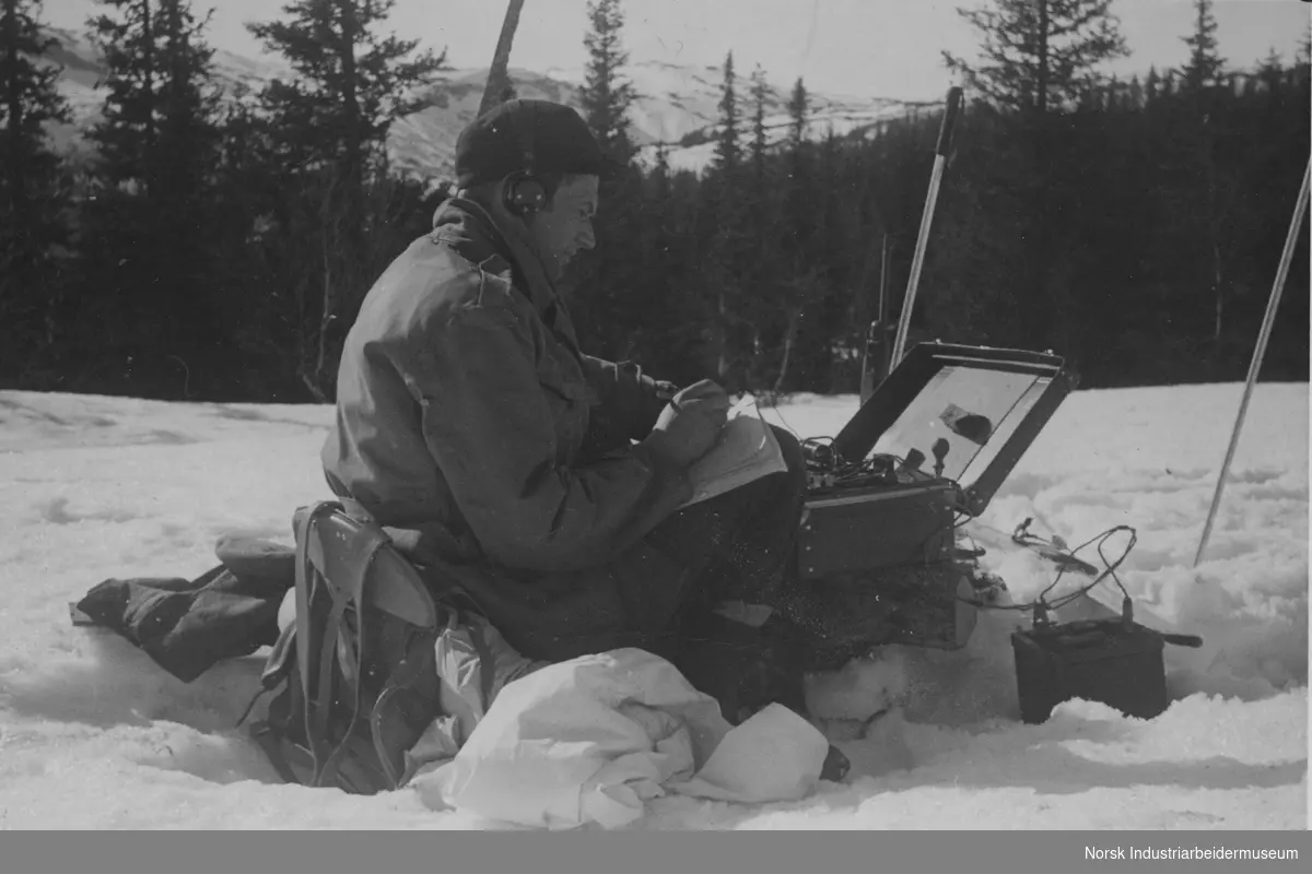Claus Helberg sittende i snøen med radiosender/mottager utenfor Sebrekke radiostasjon mars 1945