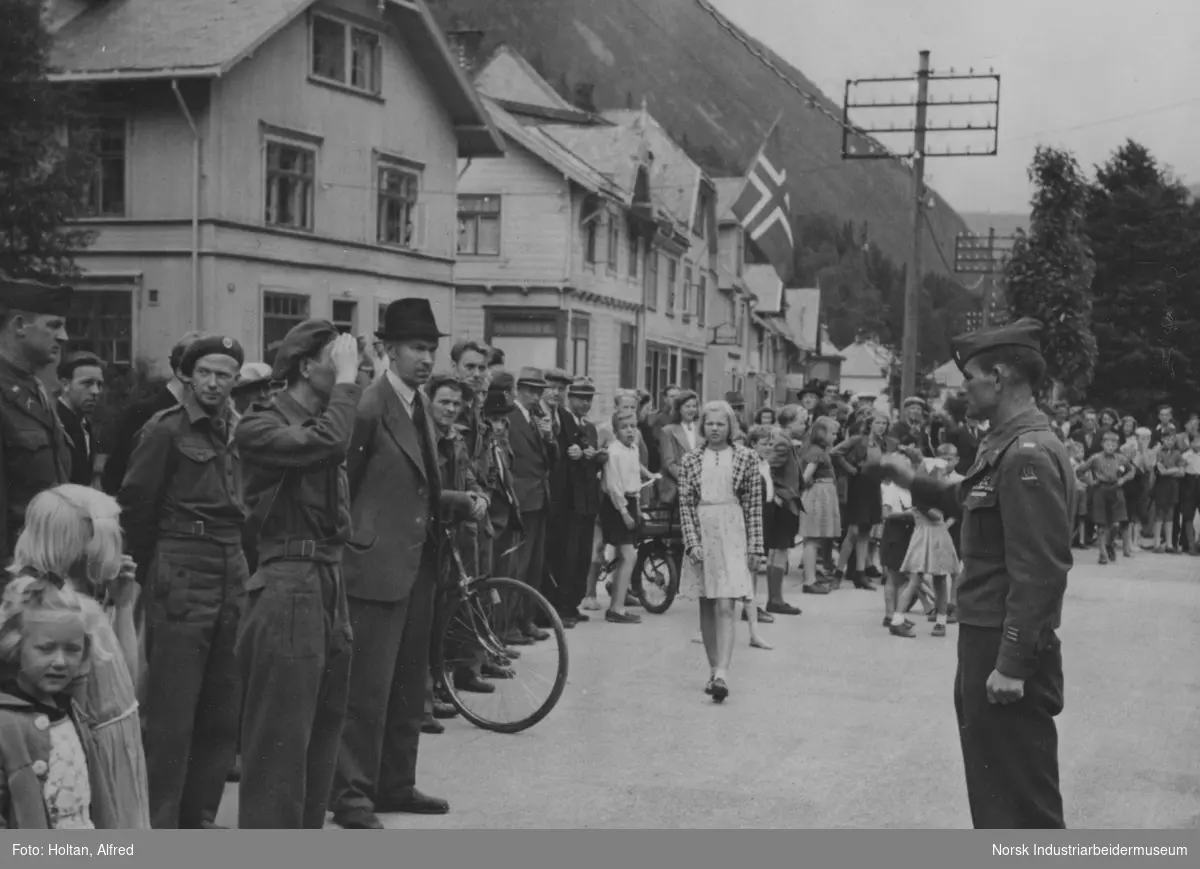 Amerikanske tropper, 474th Infantry Regimentet (Separate) på Rjukan torg etter frigjøringen. To uniformskledden menn utfører militær hilsen. Mennesker har samlet seg på torget for å se på.