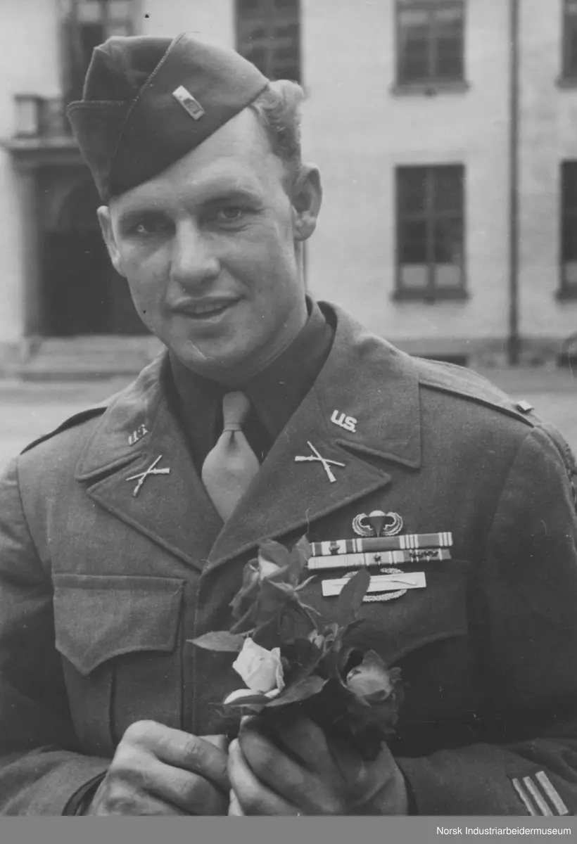 Portrett Amerikansk sersjant. Sersjanten har akkurat motatt blomster av en norsk jente på Rjukan torg. Amerikanske tropper, 474th Infantry Regimentet (Separate) besøker Rjukan etter frigjøringen. Ca. 200 amerikanske soldater på besøk på Rjukan med parade på torget.