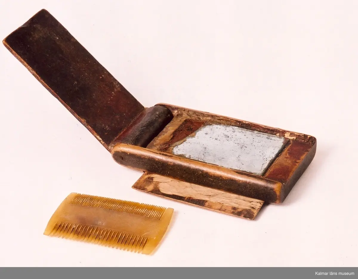 KLM 9855:1-2. Rakdon, består av borste och etui med spegel och luskam. :1 borste, längd 12 cm, diameter som mest 5 cm. :2 etui med spegel och kam, längd 11,5 cm, bredd 6,2 cm, tjocklek 1,8 cm. Borste av svinhår. Etuiets ena sida kan öppnas helt och har en spegel på insidan. Etuiets andra sidan har ett fack med skjutlock, i facket ligger en kam av ben. Dubbelkam, ena sidan kan användas som luskam.