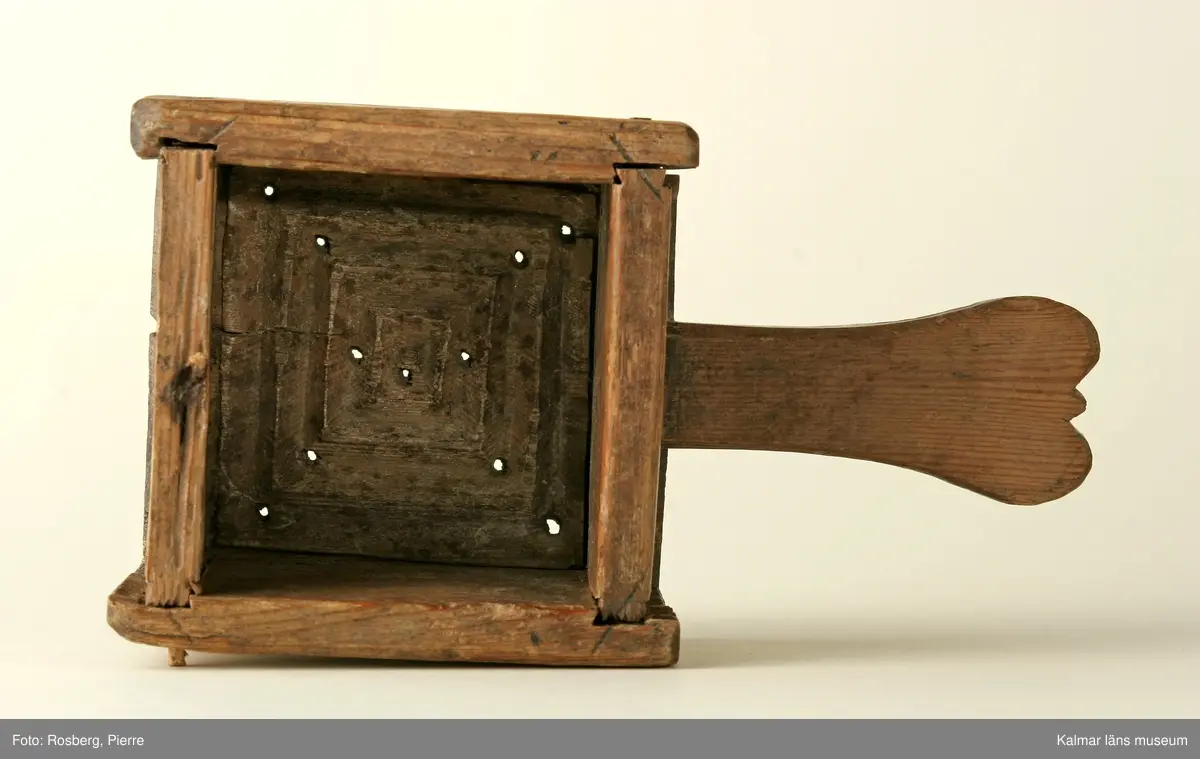 KLM 14360. Ostform. Av trä. Fyrkantig med botten utskjutande i form av ett handtag. Skuret mönster i botten, fyrkanter i varandra, minst i mitten och störst närmast kanten. Inskuren text: OS 1751.