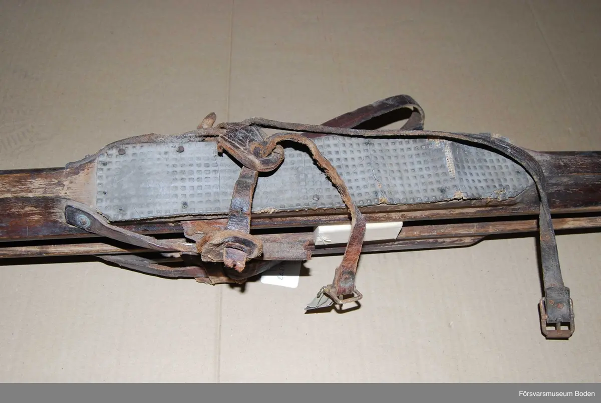 Mörkbruna skidor med låg spets och hög rygg liknande arméskidor m/1913. Fyrkantig profil på rännan undertill. Bindningar med remmar och sula av gummibelagd väv, varav den ena saknas. Den ena skidan har spruckit och reparerats med bleckplåt, men har fått en ny skada vid spetsen. Inga kronstämplar finns, däremot andra stämplar där den saknade sulan suttit. Till skidorna hör en etikett med texten "I 14/Fo 49 Museet 275".