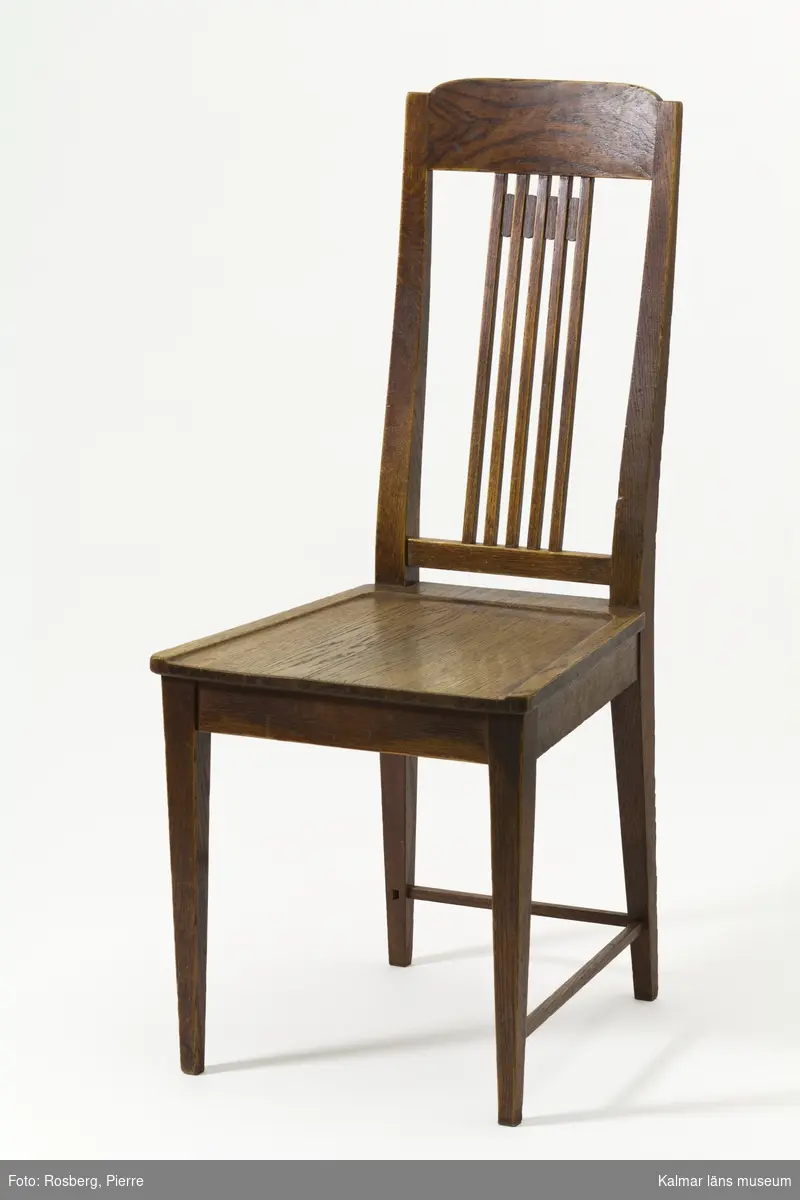 KLM 31932:1-2. Stol. 2 stycken. Av ek, träsits. Stolar med spjälrygg, ben med tunna bak- och sidoslåar. På båda stolarna är en sidoslå avbruten. Den ena stolens sits har en längsgående spricka. Stil: jugend.