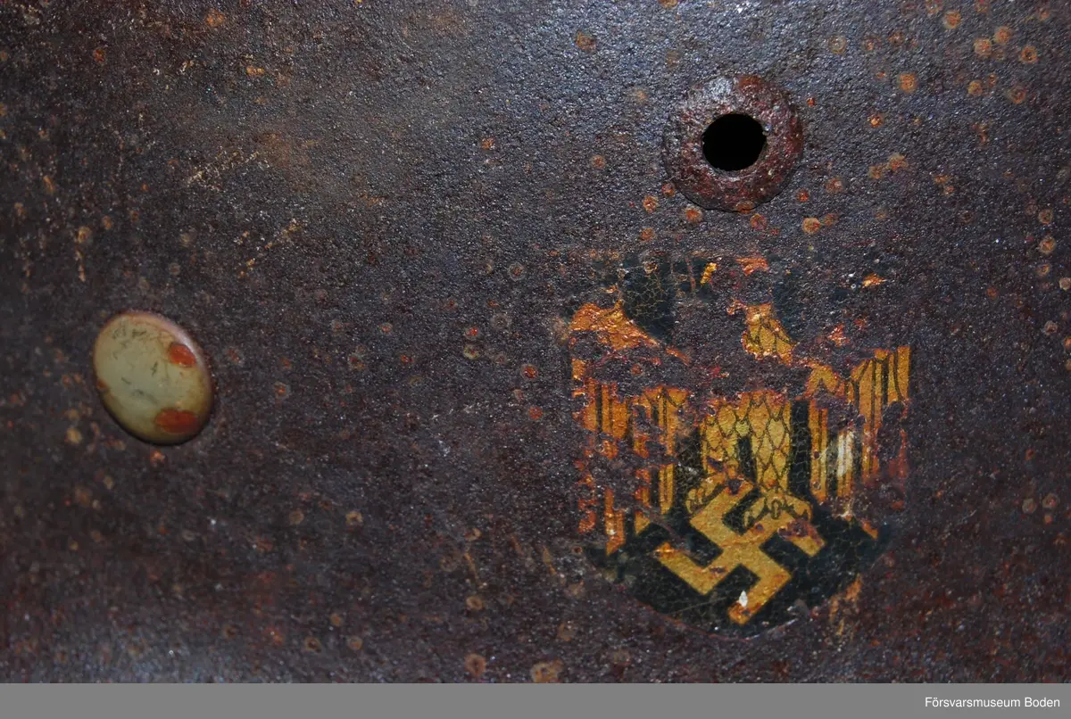 Kanten omvikt mot insidan. Inredning med aluminiumband, stämplat 1938. Rester av grön färg på insidan. Dekaler på båda sidor, varav endast rostkonturerna syns på den vänstra sidan. Storlek 59