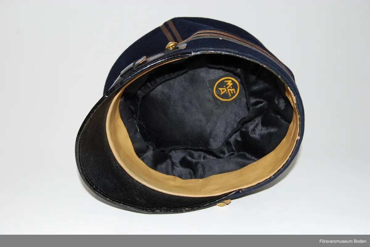 Mörkblått kläde med tre smala silvergaloner runt mössan betecknande kapten. Framtill mössmärke m/1865 med blå emalj för officererare, och ovanför detta gul sidenkokard. Mössremmen fäst på sidorna med artilleriets knapp modell mindre i guld. Buren av C.G. Dahlberg.