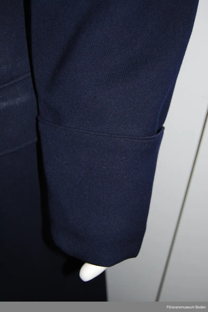 Mörkblått kläde med nervikt krage försedd med gul passpoal (nu blekt). Svart foder med kragskydd av gult kläde. Innerficka på vänster sida. Framtill två knapprader med fem knappar av artilleriets modell i guld. Fasta axelklaffar av likadant tyg som kappan med artilleriets knapp och tre metallstjärnor i guld betecknande kapten. Rundskurna ärmar med öppna uppslag som är fästa i två punkter. En ytterficka på varje sida, varav den vänstra har genomgående öppning för sabelkoppel. Skärp med två knappar på baksidan. Buren av C.G. Dahlberg.