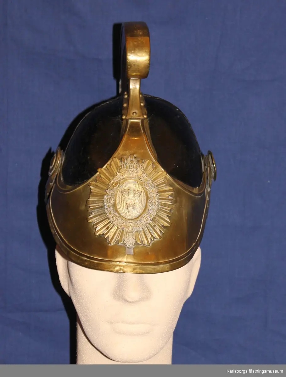 Kask m/1846, tillhörande Kavalleriet, Livregementets dragonkår. Se 6732. Avvikelser: Ingen gul sidenkokard under hakremsknappen, ovanpå kasken finns en plåtdel som går uppåt ca 7 mm och böjer sig i en båge längst fram där plymen sätts fast, kavalleriets vapenplåt.