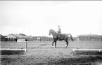 Skövde fältrittklubbs tävlingar 1932. Dressyrtävling på sandbanan öster om ridhuset. I bakgrunden järnpaddocken.
