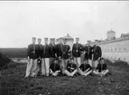 En grupp militärer med slutvärnet vid Karlsborgs fästning i bakgrunden, fotograferat i början på 1900-talet.