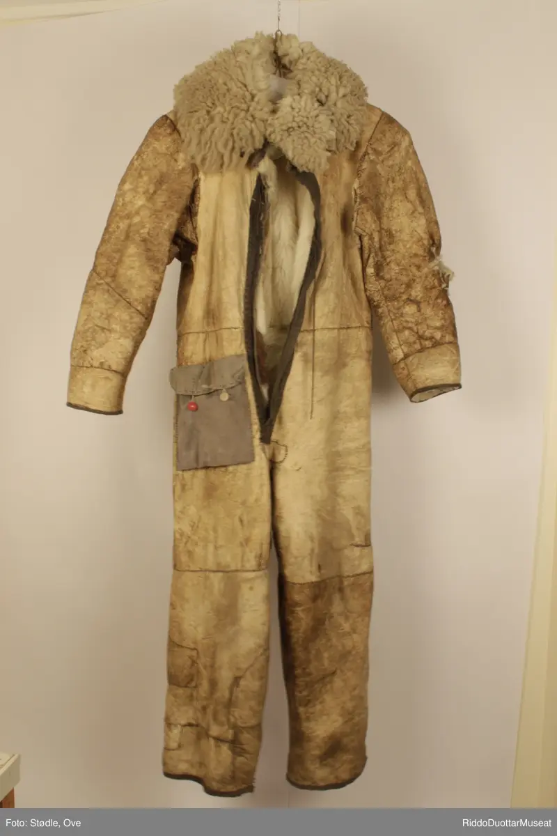 Hel dress, 173 lang. Sydd av saueskinn og sannsynligvis storfeskinn, med hårsiden innover.  Kragen er sydd av saueskinn med ullsiden ut. Glidelås-lukning. Ligner en gammel flydress. Lomme øverst på høyre lår er sydd av grått stoff, og har en rød og en brun knapp.